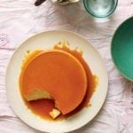 A classic flan de leche on a white plate, covered with caramel and a spoonful of custard missing from the flan.