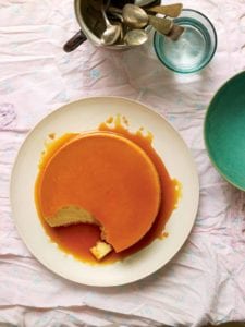A classic flan de leche on a white plate, covered with caramel and a spoonful of custard missing from the flan.