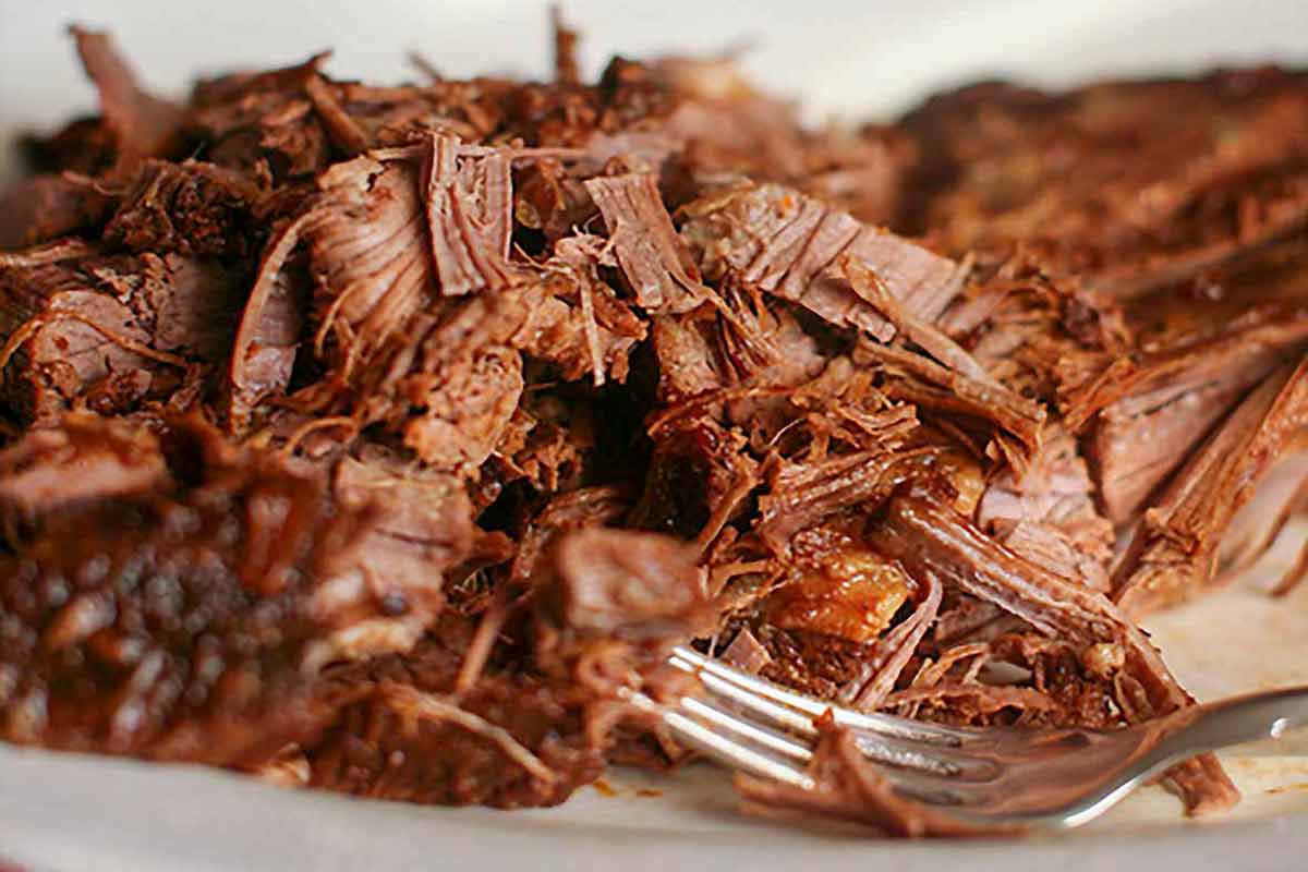 A plate of shredded Coca-Cola brisket with a fork resting in the meat.