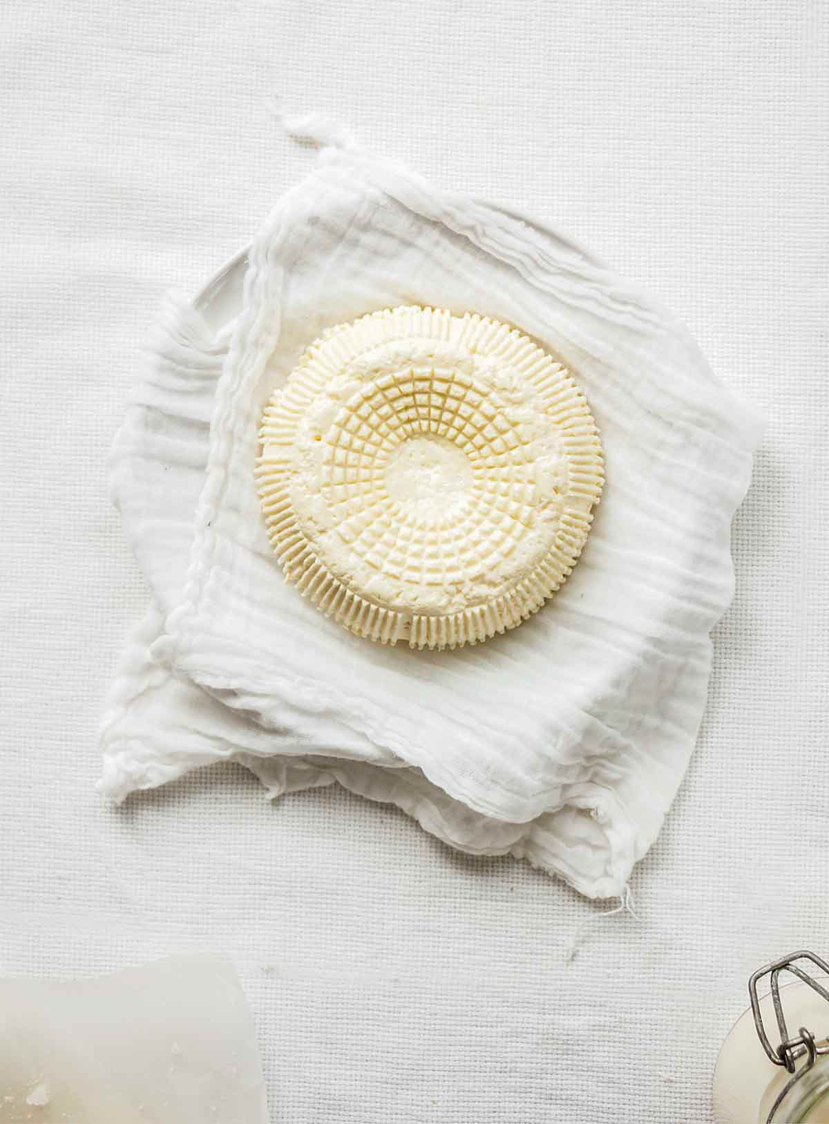 A round of farmers cheese resting on a piece of cheesecloth in a bowl.