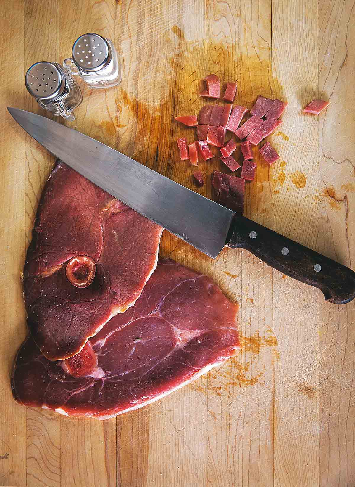 A slice of ham with red eye gravy on a cutting board with a knife and salt and pepper shaker.