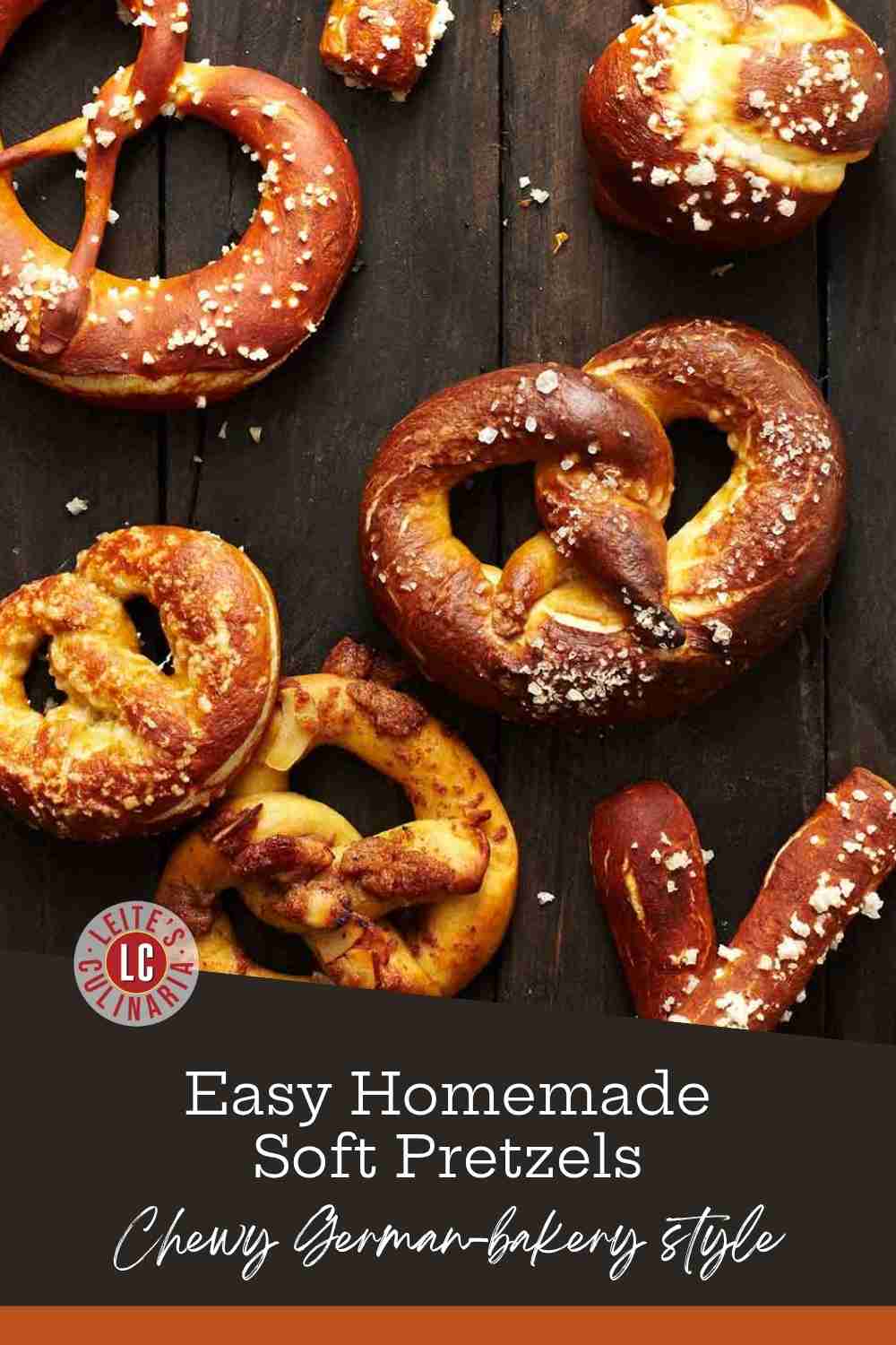 Deep mahogany soft pretzels and pretzel bites covered in coarse sea salt on a dark, rustic wooden surface.