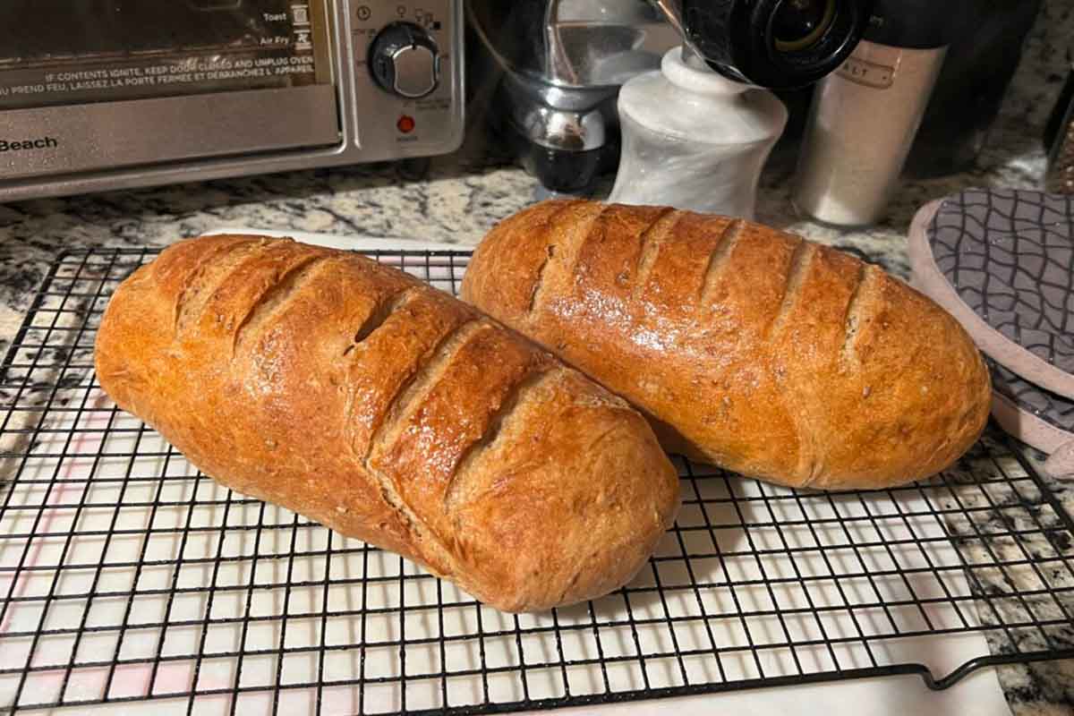 Two gorgeous loaves of Jewish rye bread with scored tops on a wire cooling rack.