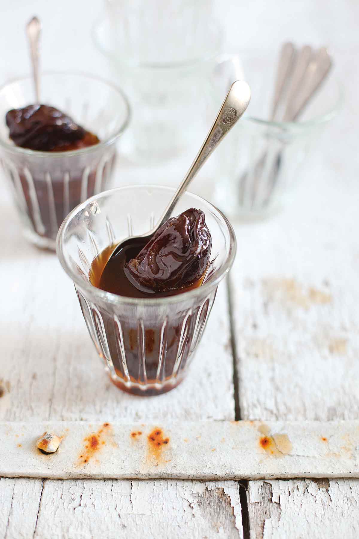 Two small glasses filled with prunes in rum and a spoon resting inside each glass.
