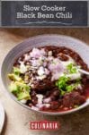 A white bowl filled with beef and black bean chili, topped with red onion, avocado, queso fresco, and diced jalapeno