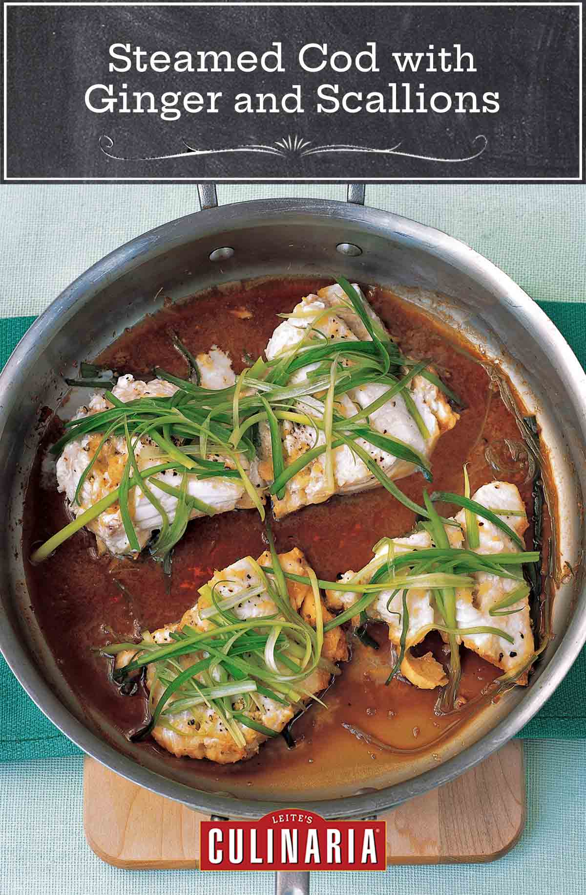 A metal skillet with four pieces of steamed cod with ginger and scallions.