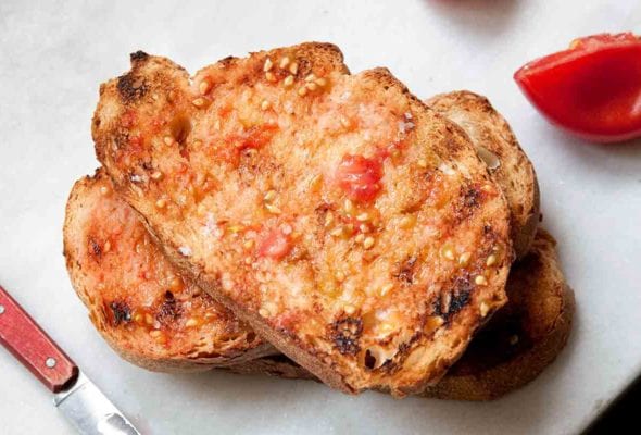 Two slices of tomato rubbed bread and three tomato halves that have been rubbed on the bread.
