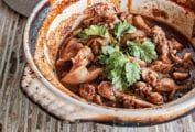 Clay pot filled with Vietnamese caramel chicken pieces and cilantro on a wooden table