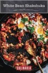 Cast iron skillet with white bean shakshuka--whit beans, tomatoes, feta cheese, eggs, and parsley