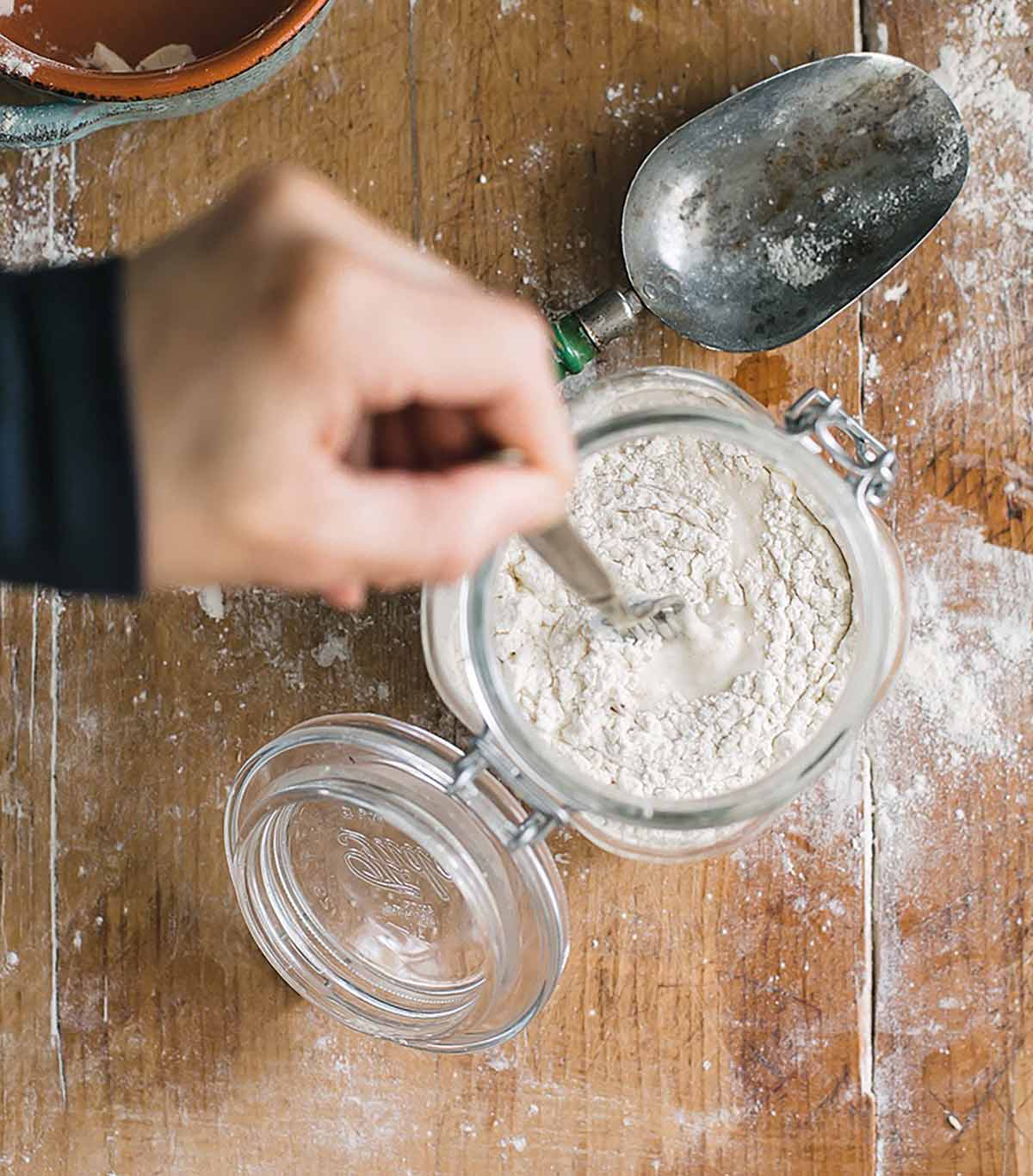 A person stirring additional flour into a starter as part of an explanation on how to make sourdough starter.