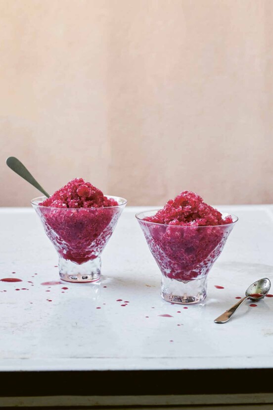 Two small glass dishes of blood orange granita, one with a spoon in it and the other with a spoon resting beside it.