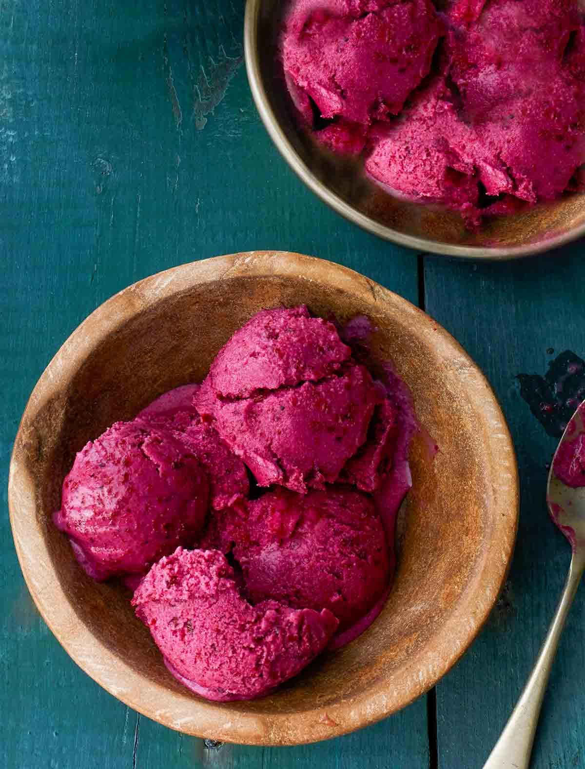 Four scoops of blueberry frozen yogurt in a wooden bowl with a spoon resting beside it.