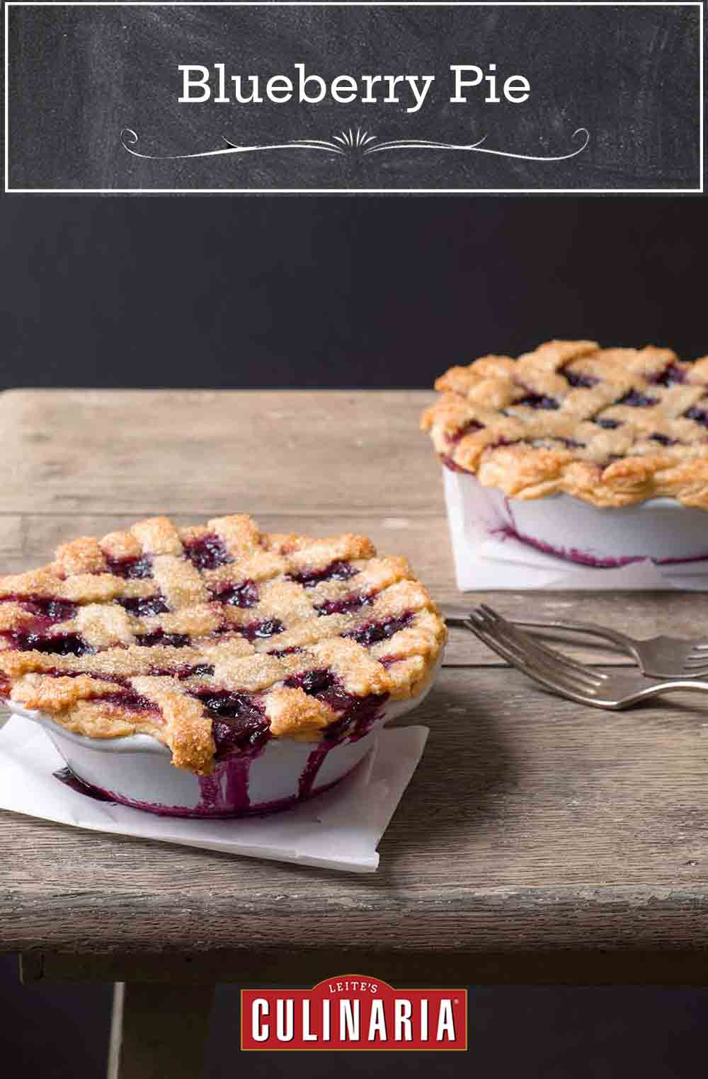 Two individual size blueberry pies on a wooden table.