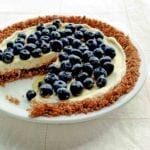 A blueberry pie with granola crust and blueberries on top with one slice missing.
