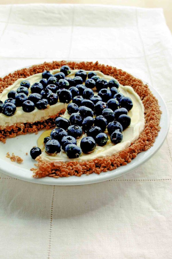 A blueberry pie with granola crust and blueberries on top with one slice missing.