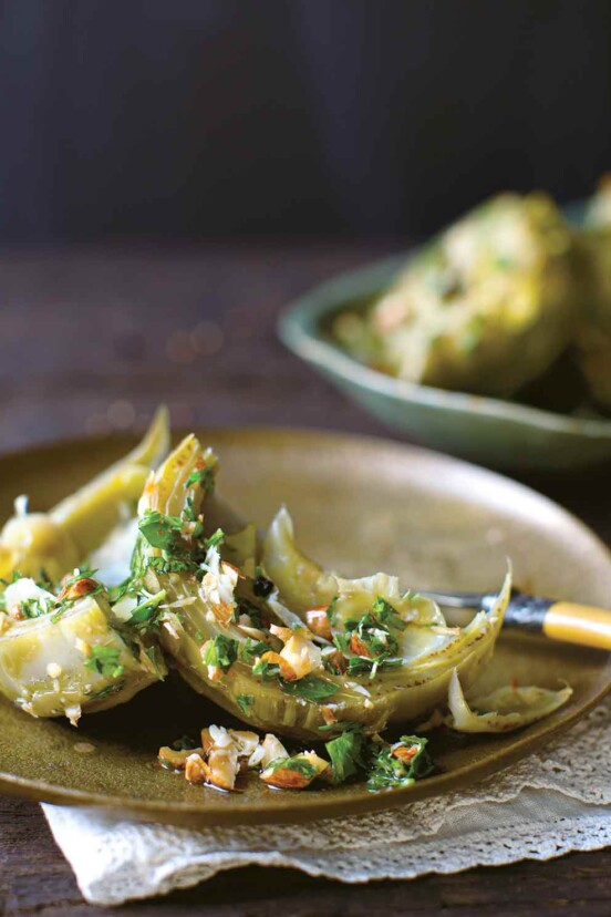 Braised artichokes on a plate, sprinkled with chopped almonds and parsley.