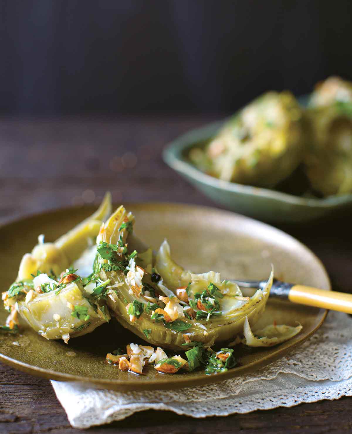 Braised artichokes on a plate, sprinkled with chopped almonds and parsley.