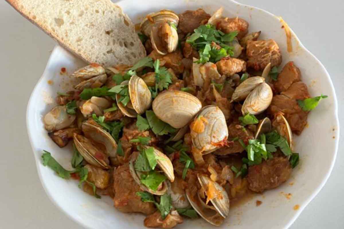 A white bowl filled with marinated and braised pork chunks and clams over cubed potatoes.