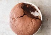 A partially-eaten chocolate souffle in a round white ceramic dish.