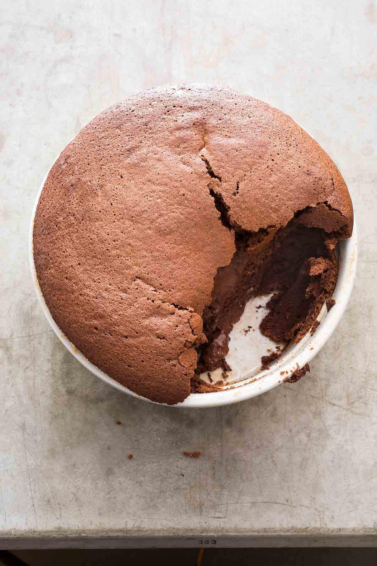 A partially-eaten chocolate souffle in a round white ceramic dish.