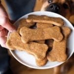 A person holding a white platter filled with homemade dog treats and a dog looking at them.