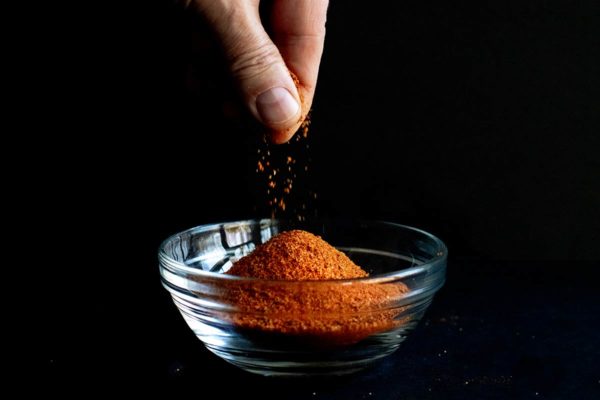 A hand sprinkling homemade Old Bay Seasoning in a small glass bowl