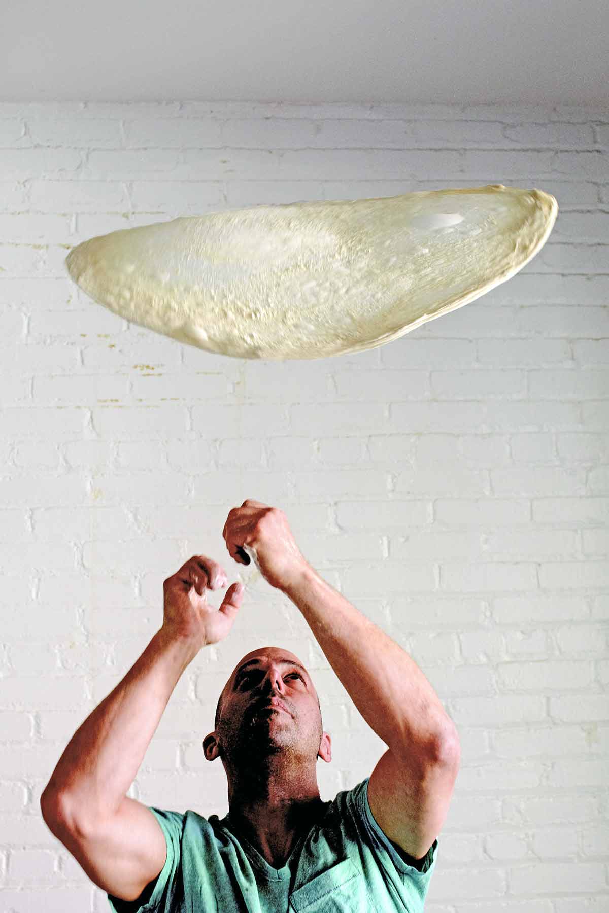 A thin circle of stretched pizza dough being tossed in the air.