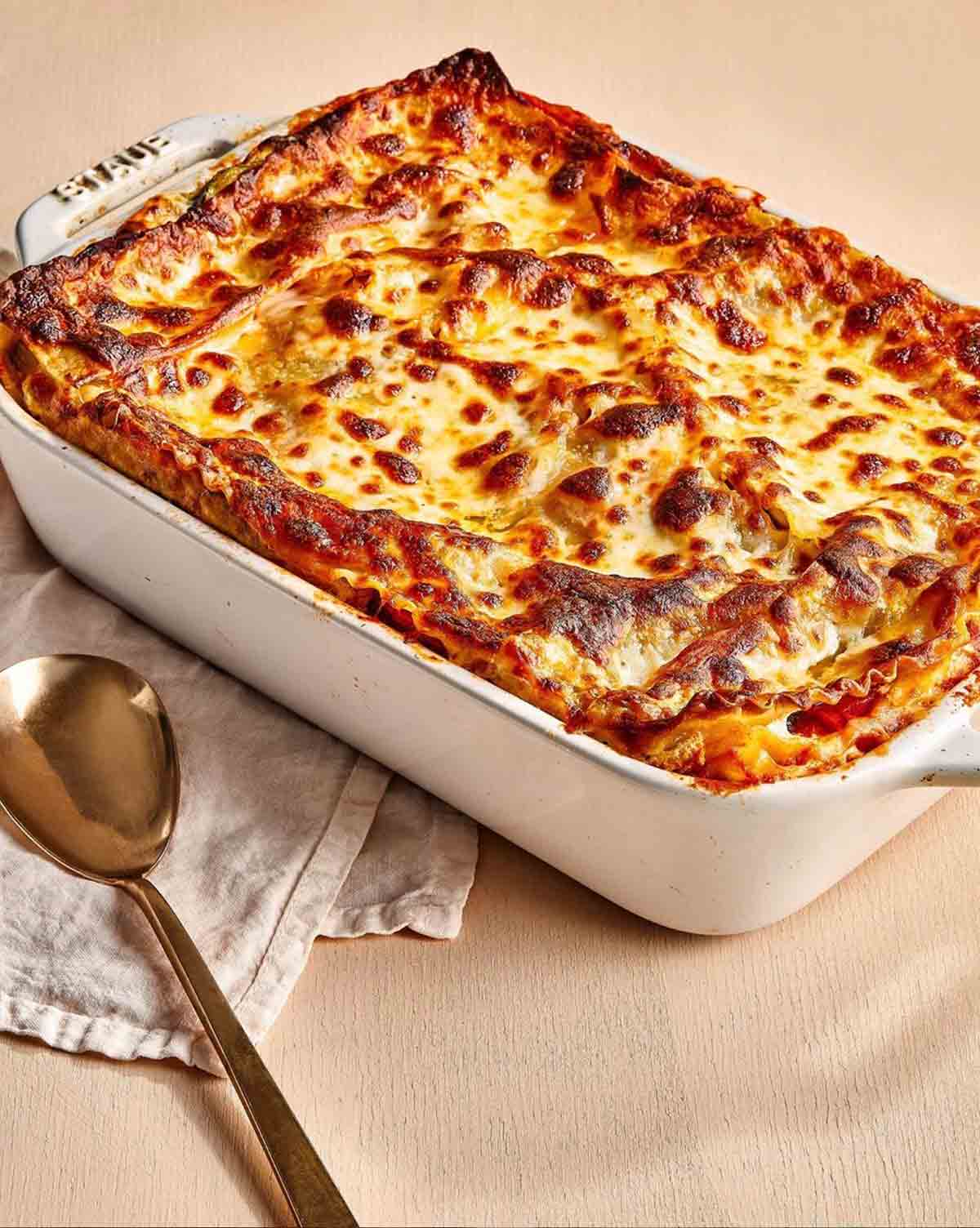 A white casserole dish filled with a cooked lasagne.