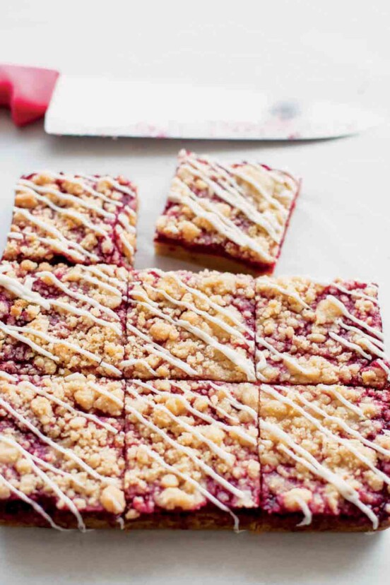 A batch of raspberry Linzer bars cut into nine squares, with one square missing and a knife in the background.