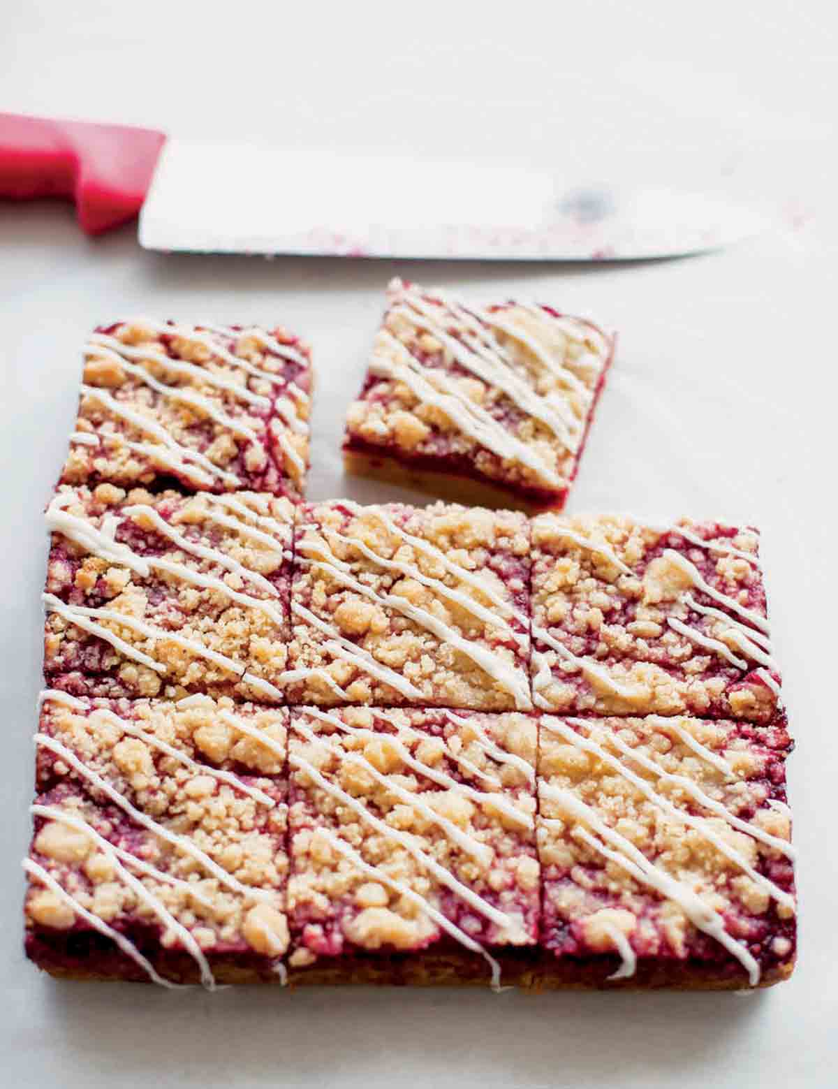 A batch of raspberry Linzer bars cut into nine squares, with one square missing and a knife in the background.