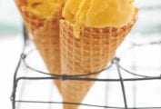 Two waffle cones filled with mango frozen yogurt propped up in a metal rack.
