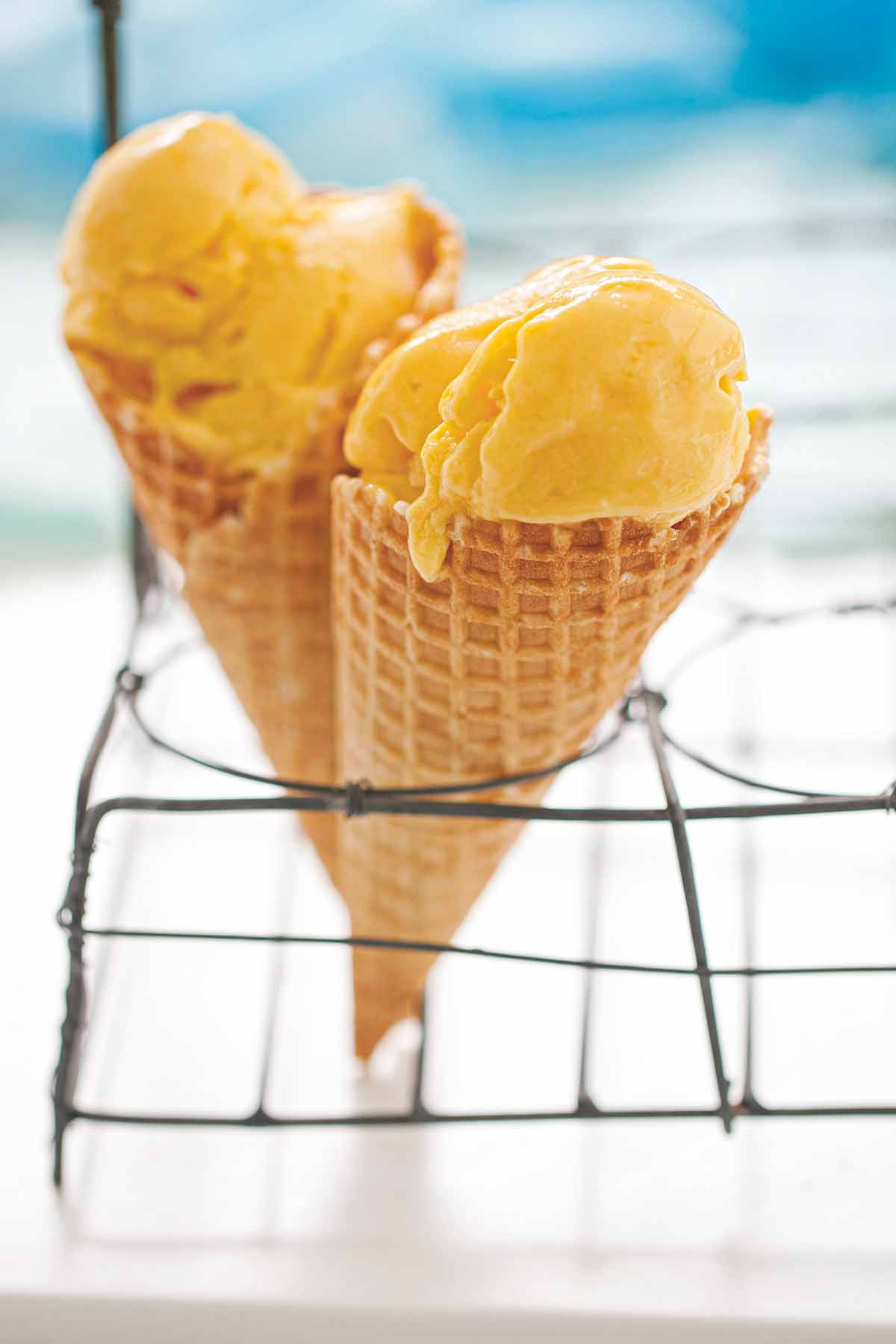 Two waffle cones filled with mango frozen yogurt propped up in a metal rack.