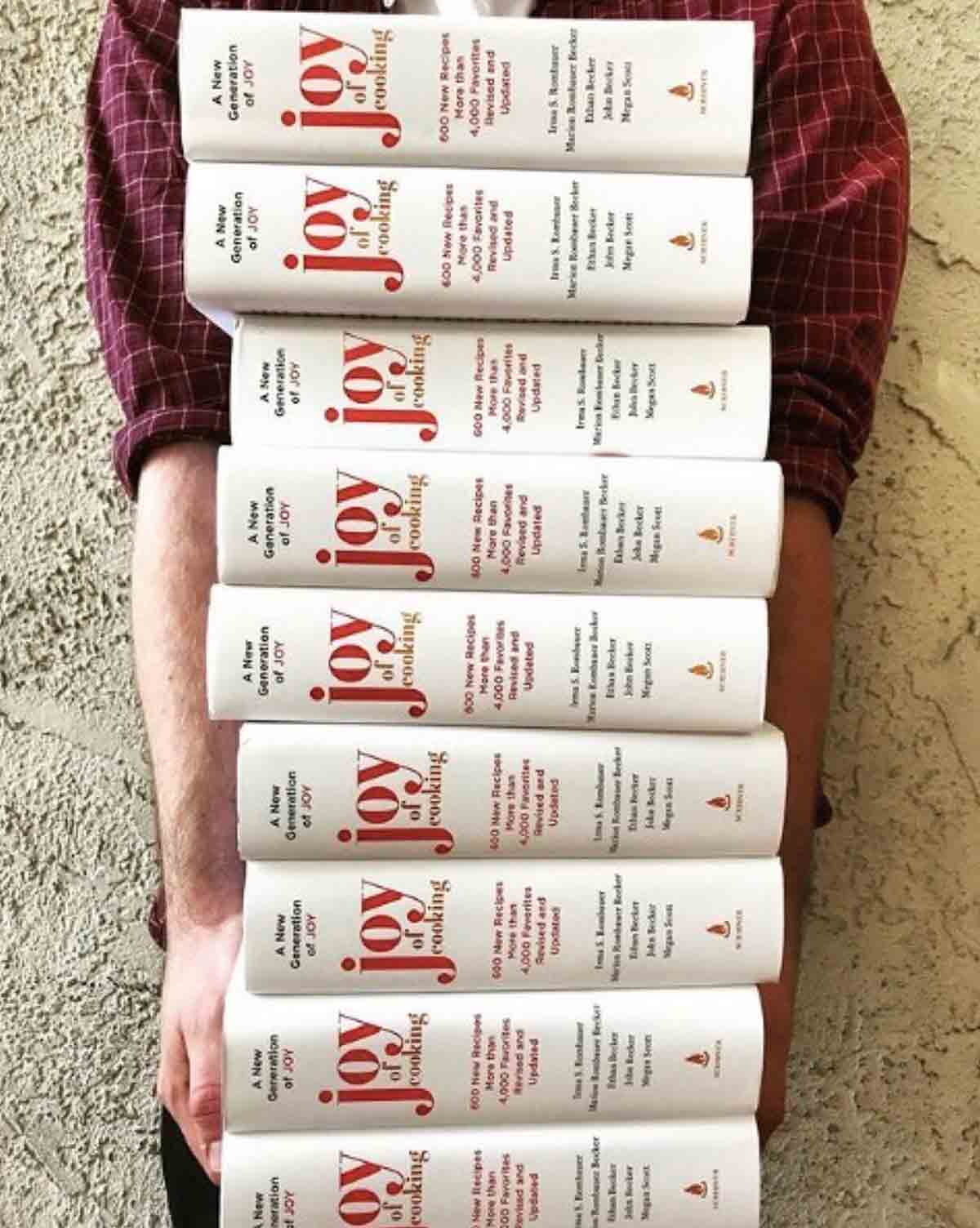 A person holding a stack of Joy of Cooking books.