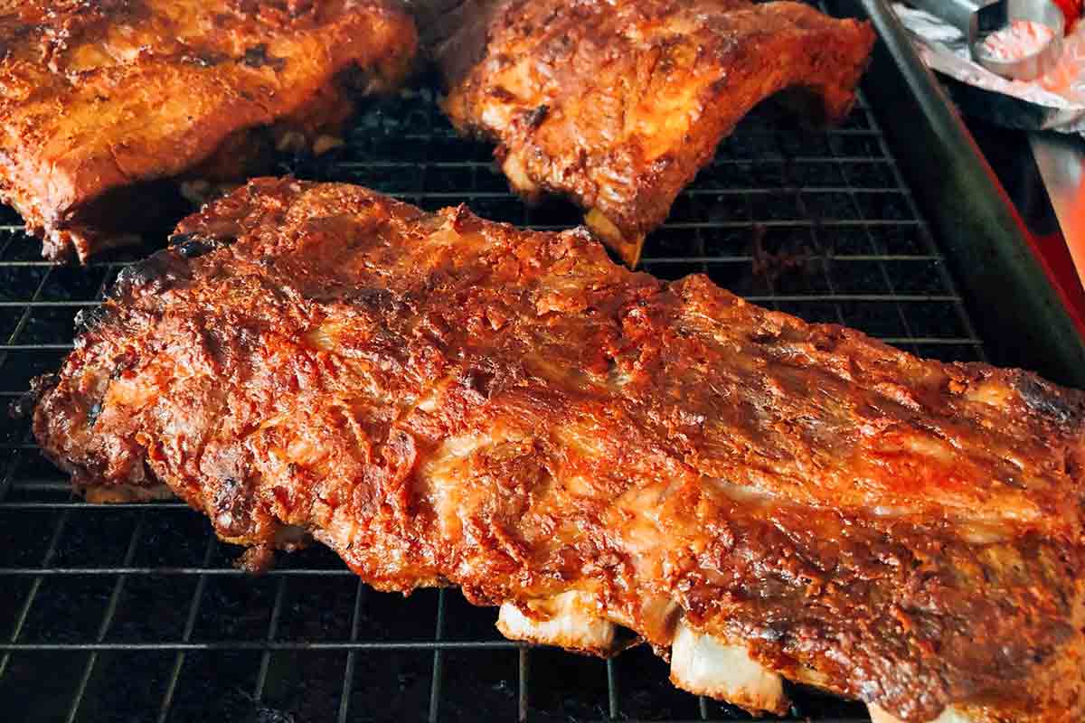 Four slabs of BBQ oven ribs on a rack inside a rimmed baking sheet.