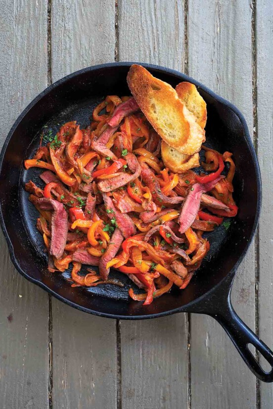Skillet steak peperonata and two slices of toasted baguette in a cast-iron pan.
