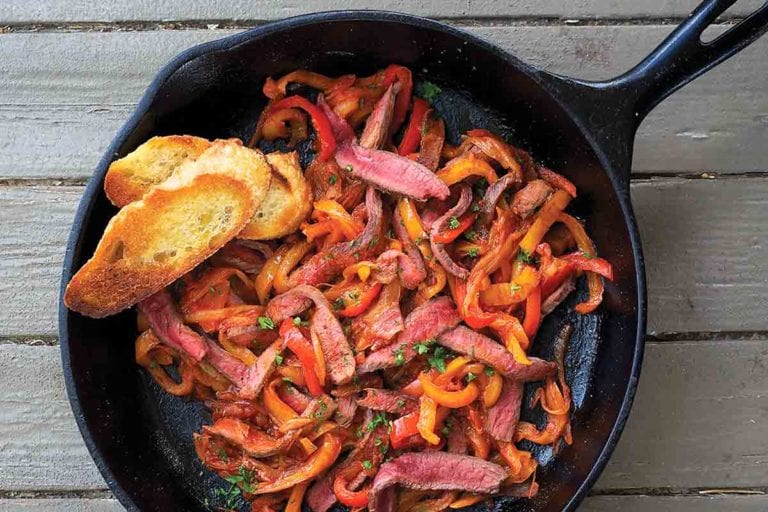 Skillet steak peperonata and two slices of toasted baguette in a cast-iron pan.