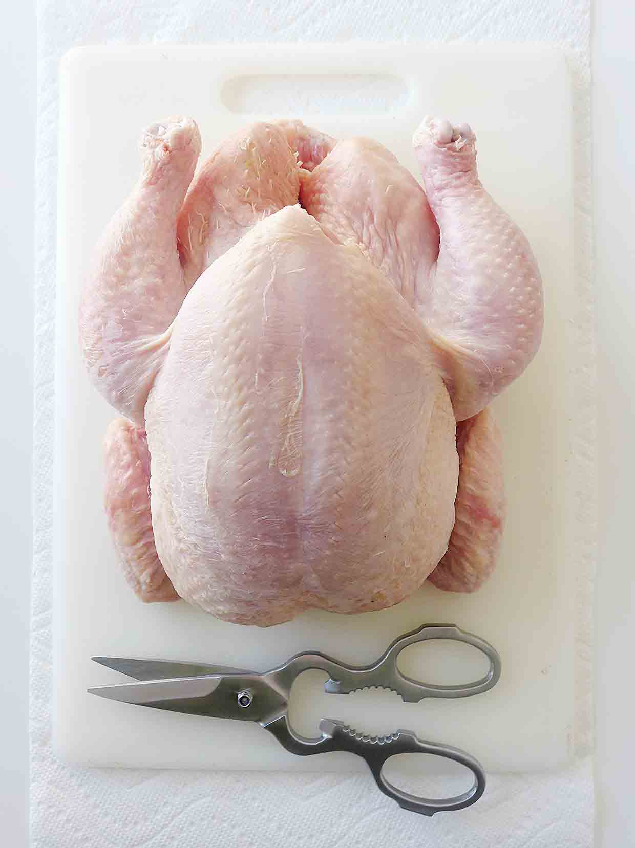 A whole chicken on a cutting board with a pair of kitchen shears beside it.