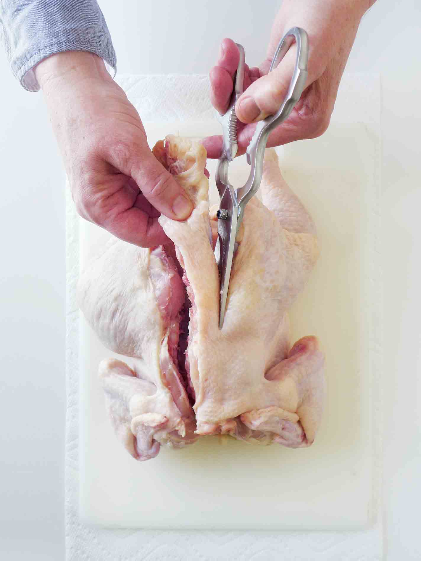 A person cutting through the backbone of a chicken to spatchcock it.