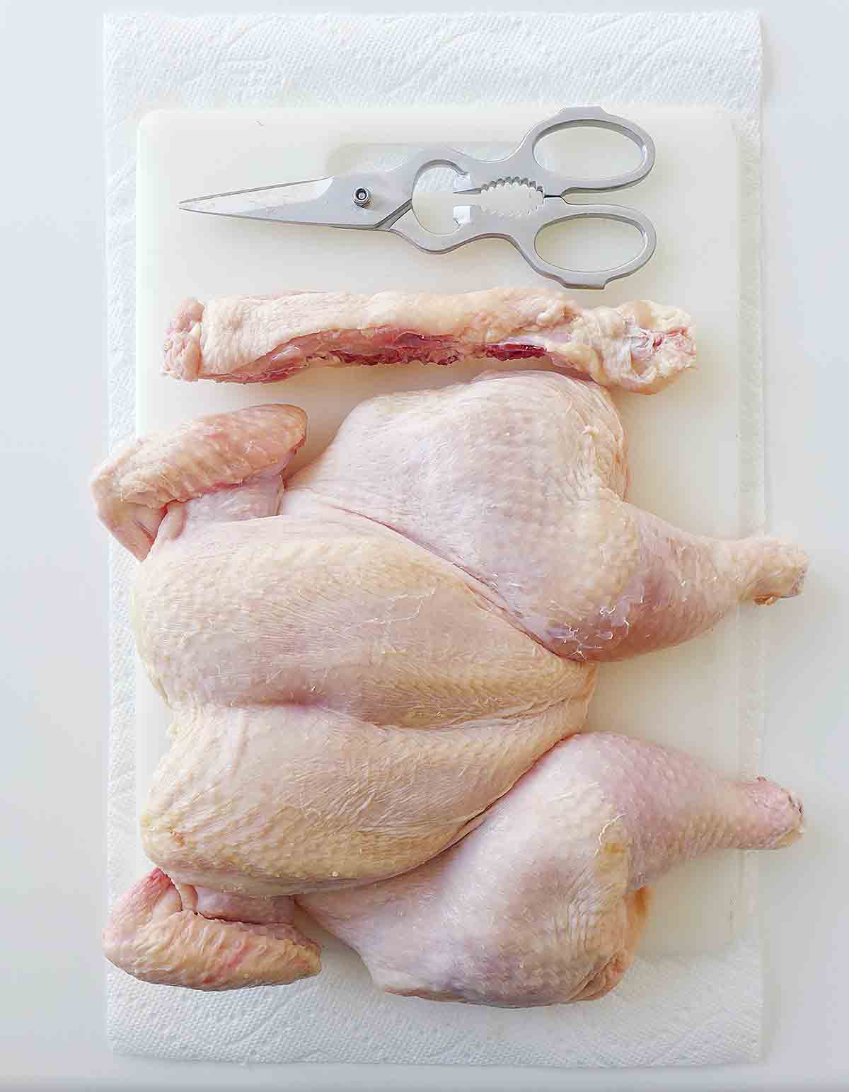 A finished spatchcocked chicken on a cutting board with a pair of kitchen shears beside it.