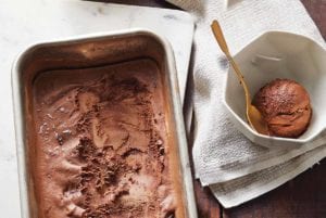 A metal dish filled with vegan chocolate fudge swirl ice cream, as well as two bowls with gold spoons, one empty and one with a scoop of ice cream.