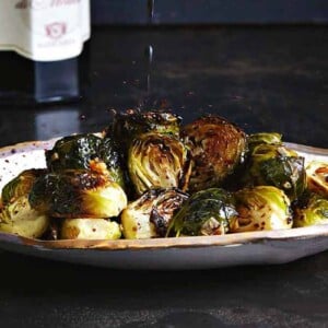 A plate of roasted Brussels sprouts with a drizzle of balsamic vinegar splashing down on it