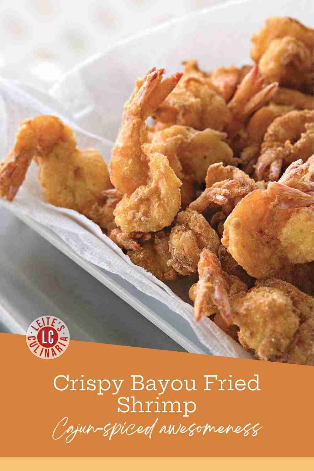 Golden brown fried shrimp with tails on, resting on white paper towels in a metal tray.