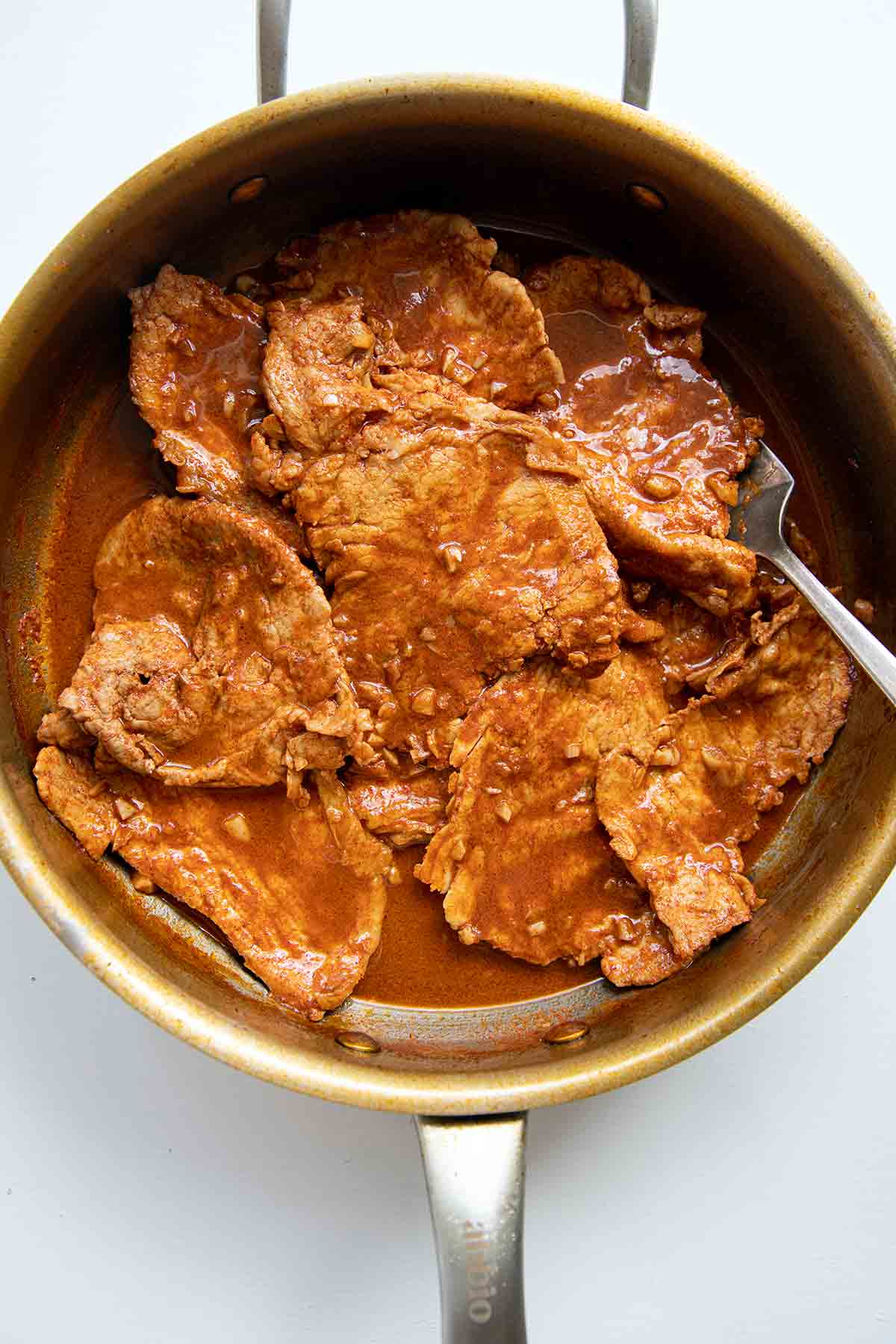 Thin slices of pork in a pot that are being cooked for bifanas.