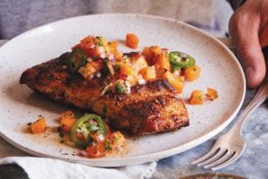 A person sitting in front of a plate of blackened grouper with peach jalapeño salsa.