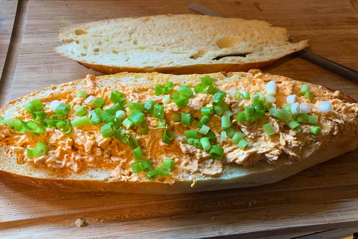 A loaf of Italian bread filled with buffalo chicken dip, garnished with scallions.