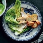 A blue and white plate topped with a deconstructed chicken Caesar salad with baguette round croutons.