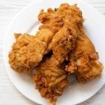 Three pieces of cornmeal-crusted fried chicken on a white plate.