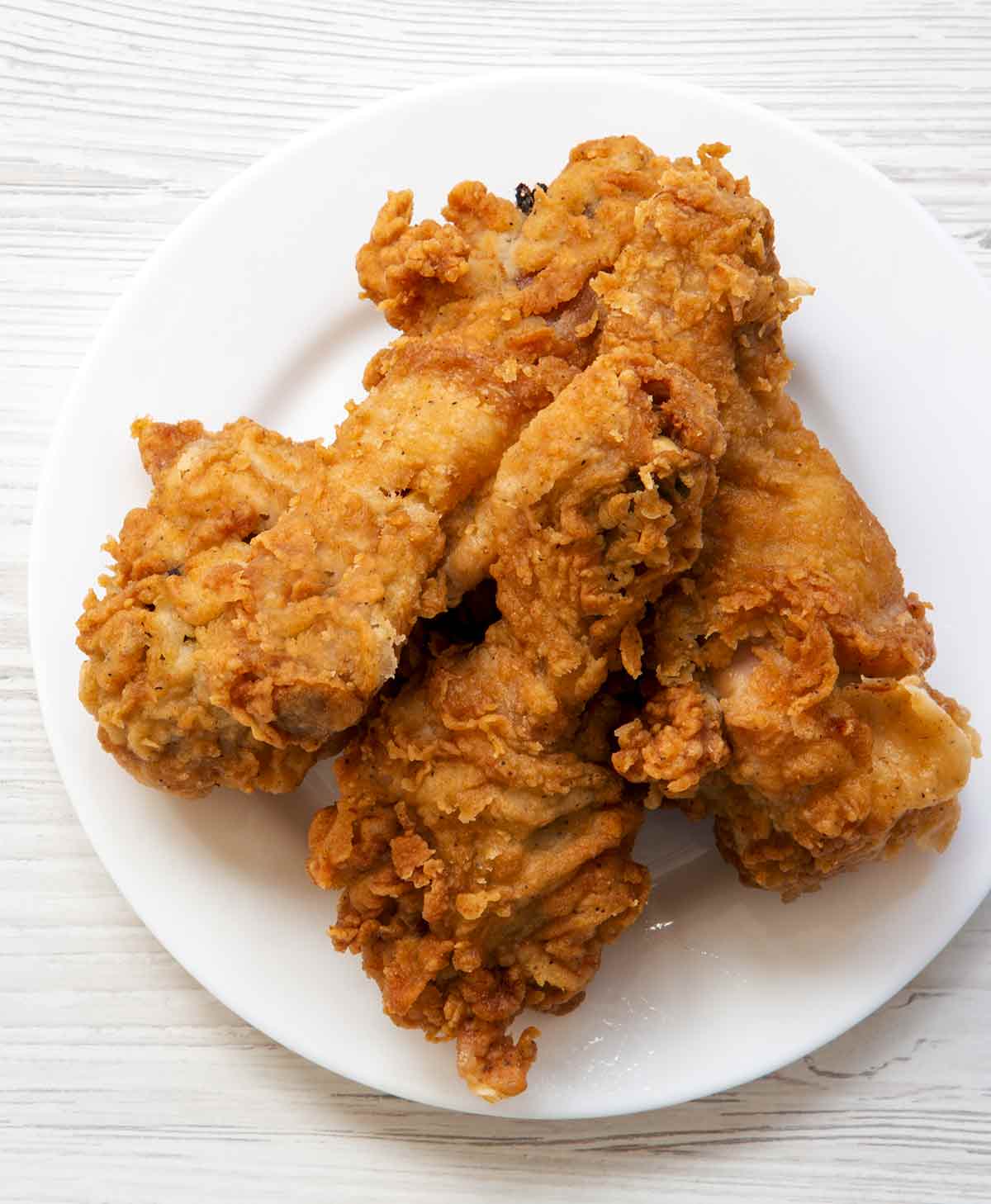 Three pieces of cornmeal-crusted fried chicken on a white plate.