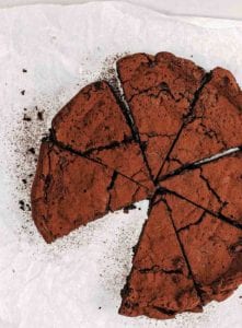 A flourless chocolate chile cake cut into 8 wedges with one slice missing on a piece of parchment paper.