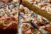 A baked loaf of focaccia with red onion and rosemary with two wedges cut from it.